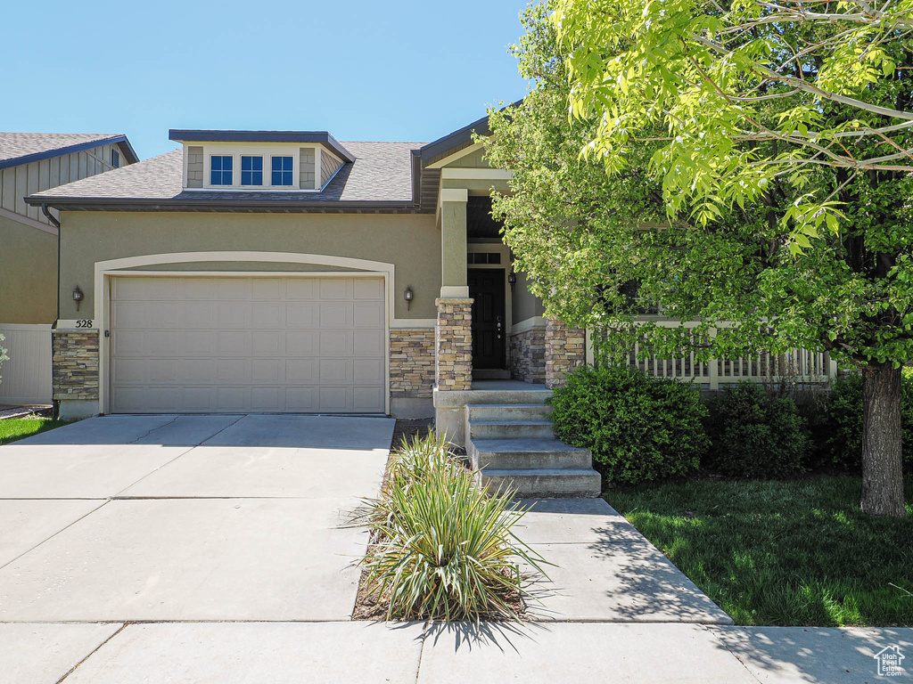 View of front facade with a garage, stone siding, roof with shingles, stucco siding, and driveway