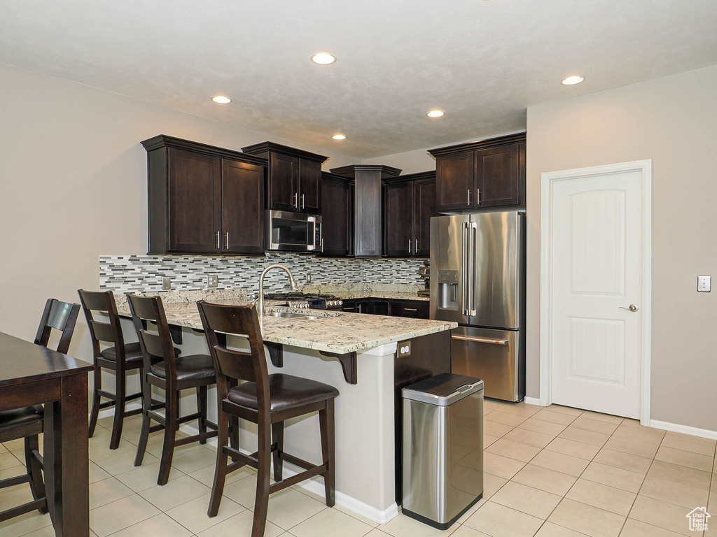 Kitchen with a peninsula, appliances with stainless steel finishes, a kitchen bar, and tasteful backsplash