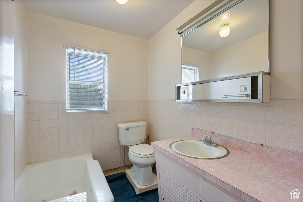 Full bathroom with a bathtub, toilet, tile walls, vanity, and wainscoting
