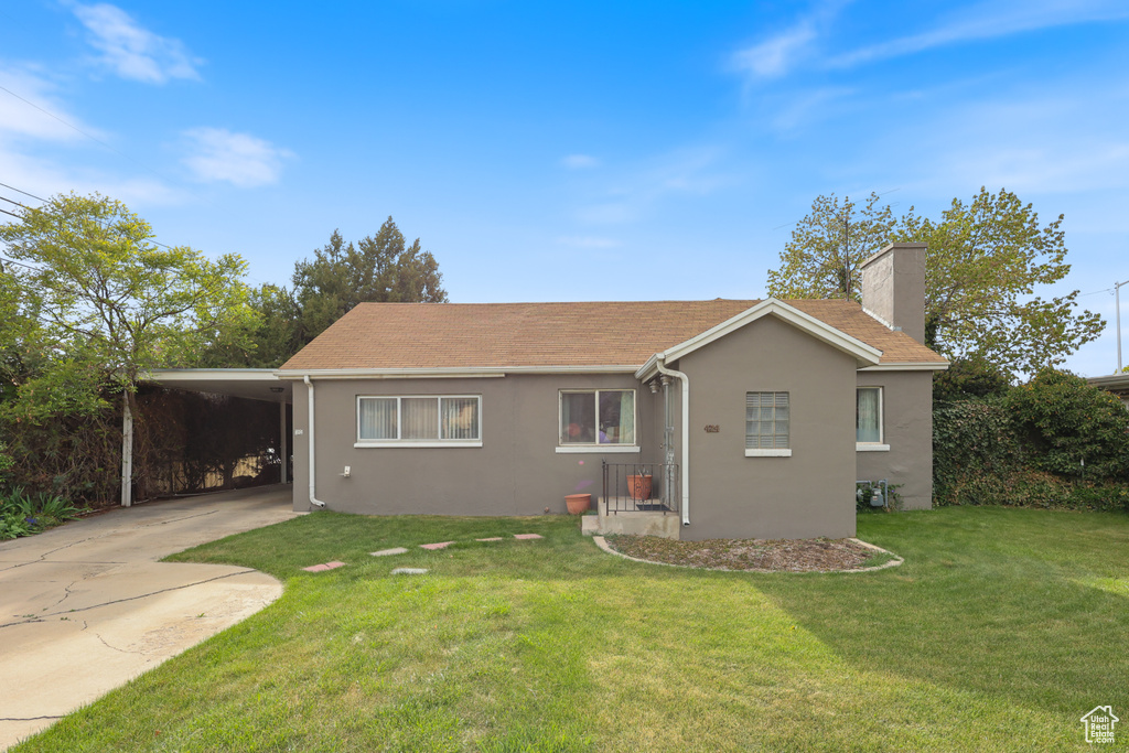 Back of property with a lawn, driveway, a carport, a chimney, and stucco siding