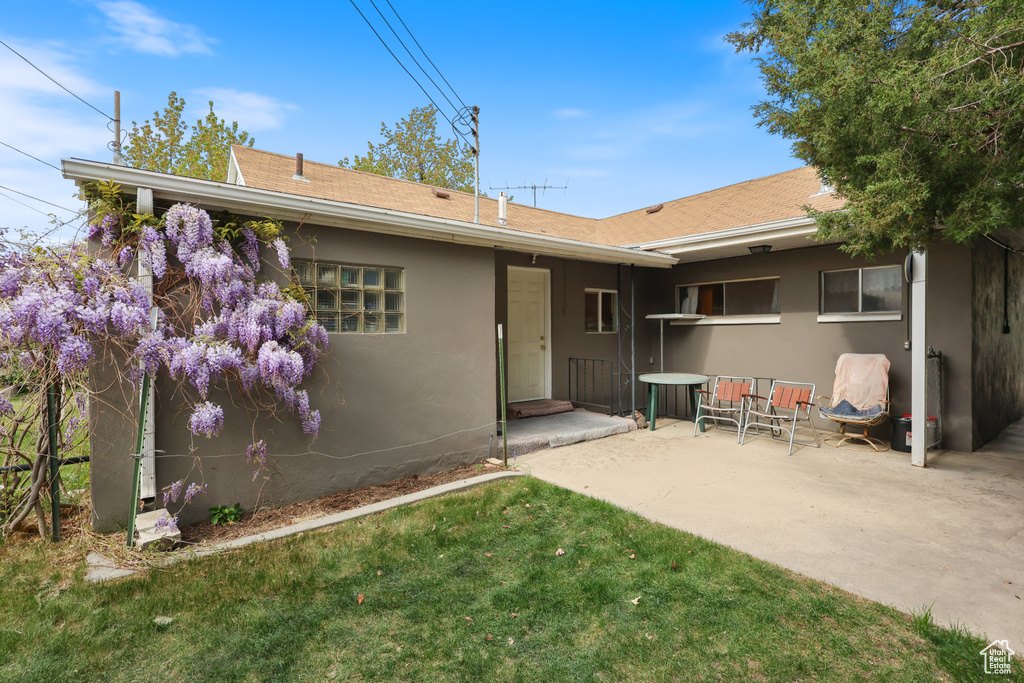 Back of property with a lawn, roof with shingles, stucco siding, and a patio area