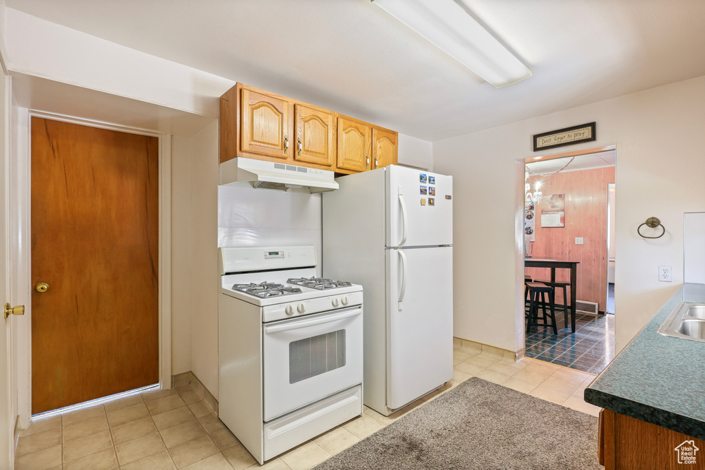 Kitchen featuring light tile patterned floors, a sink, under cabinet range hood, and white appliances