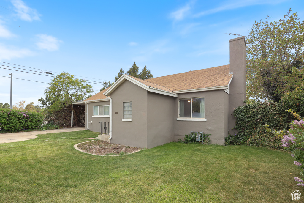 View of home\'s exterior with stucco siding, a chimney, a lawn, and concrete driveway