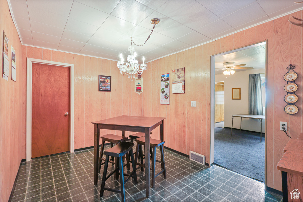 Dining space featuring dark floors, visible vents, wooden walls, ornamental molding, and ceiling fan with notable chandelier