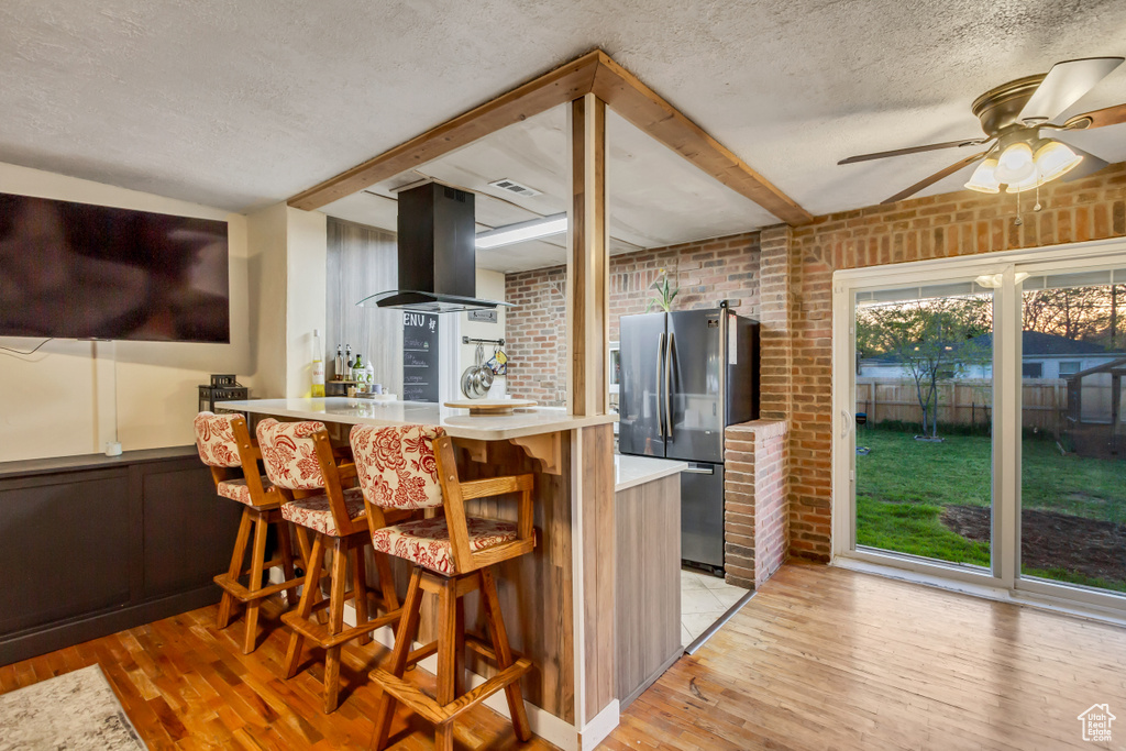 Kitchen with island exhaust hood, freestanding refrigerator, light wood finished floors, and ceiling fan