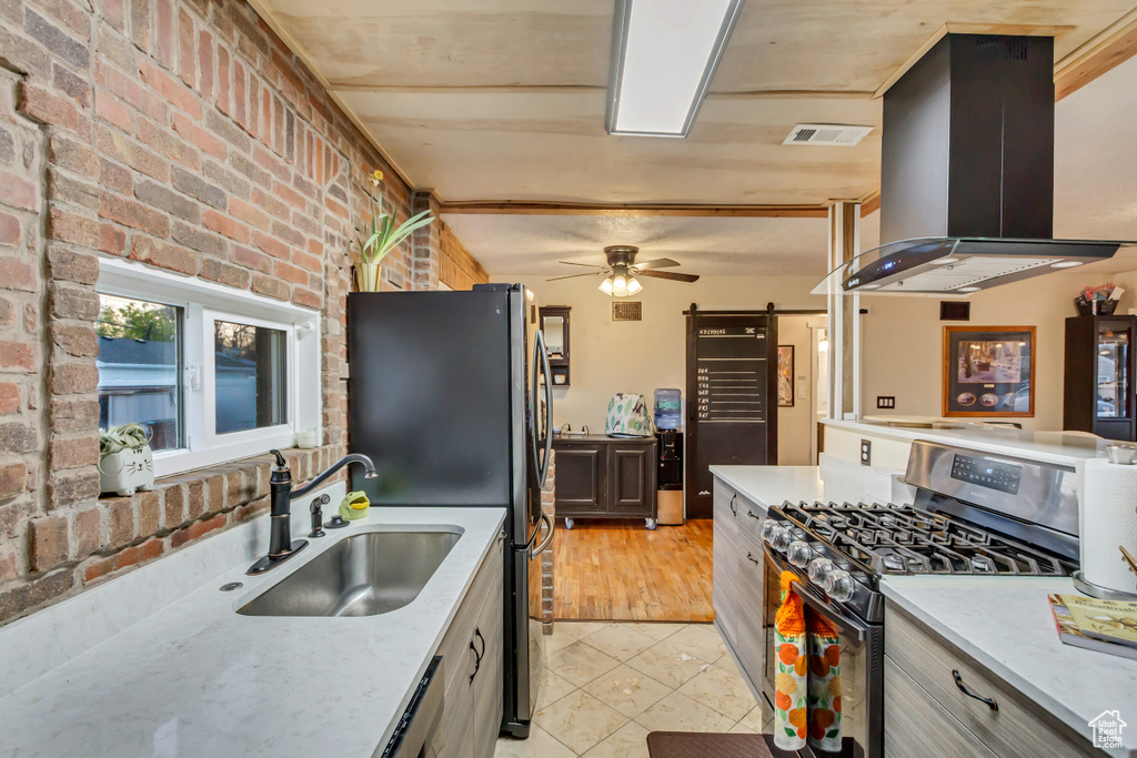 Kitchen featuring brick wall, island exhaust hood, a sink, light tile patterned floors, and stainless steel appliances