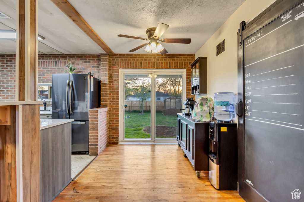 Kitchen with freestanding refrigerator, brick wall, ceiling fan, a barn door, and light wood finished floors