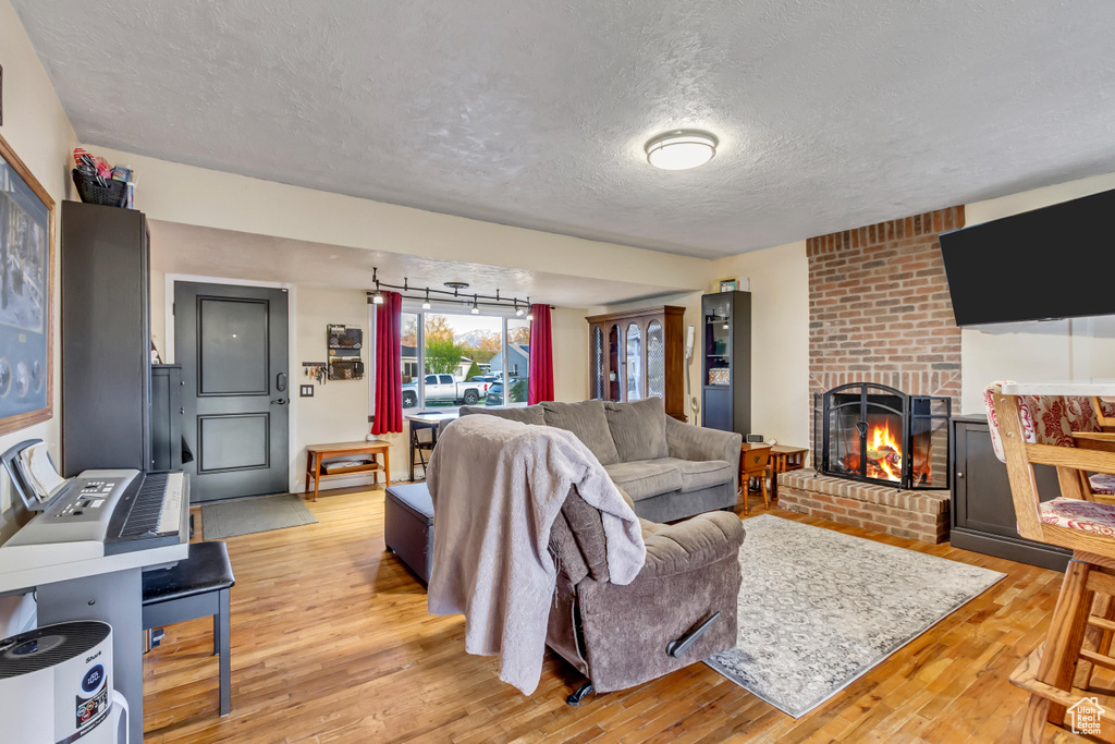 Living room with a brick fireplace, light wood finished floors, and a textured ceiling