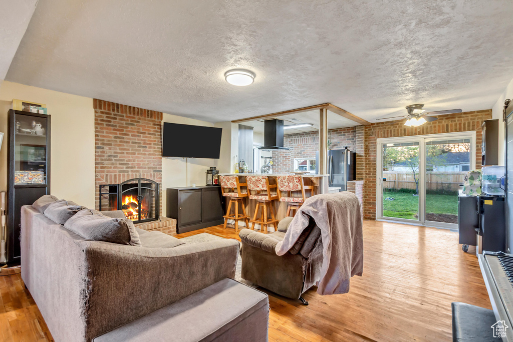 Living area featuring brick wall, ceiling fan, light wood finished floors, and a fireplace