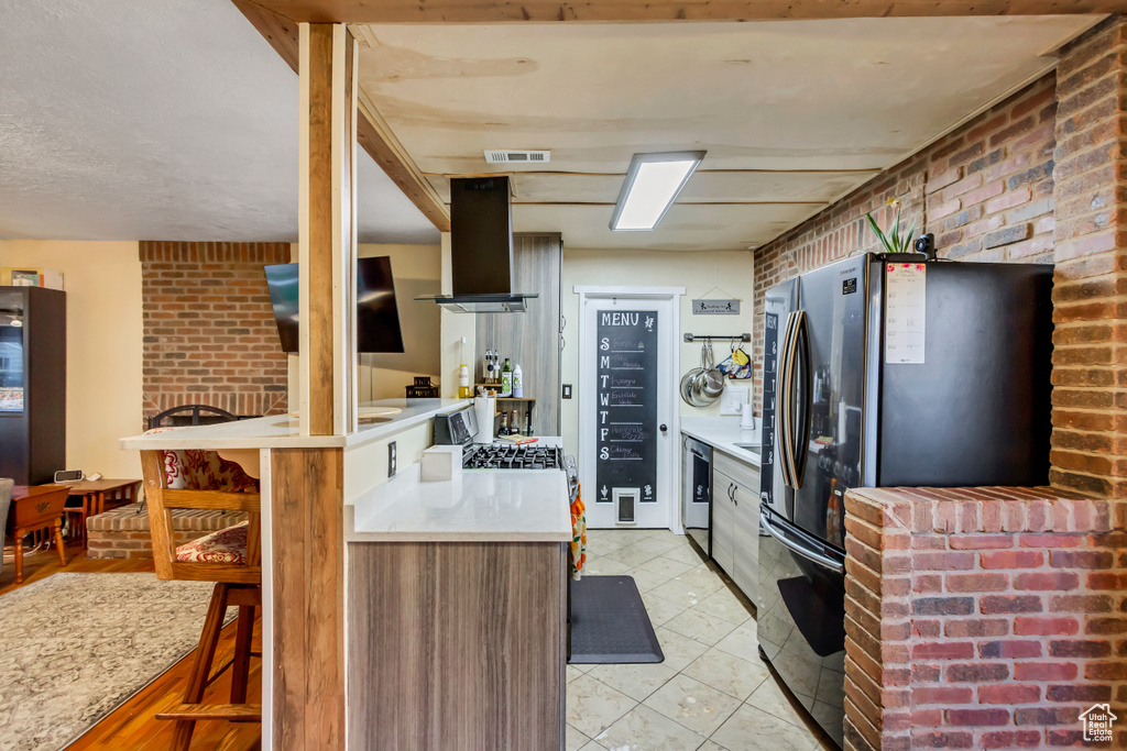 Kitchen featuring visible vents, freestanding refrigerator, brick wall, light countertops, and island exhaust hood
