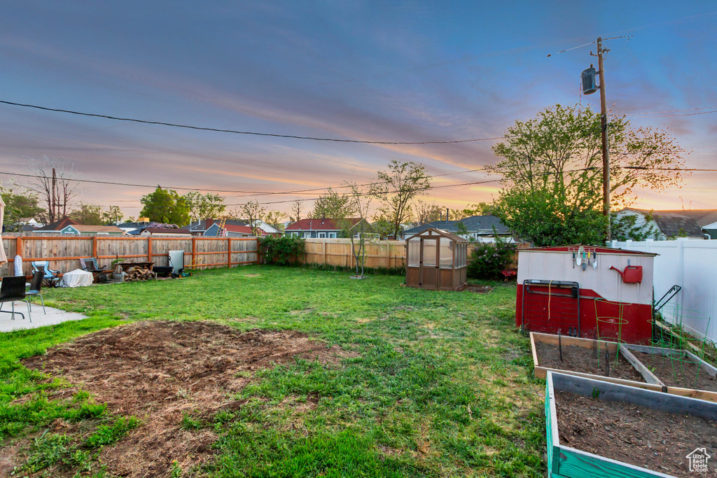 Yard at dusk with a fenced backyard, an outdoor structure, an exterior structure, and a garden