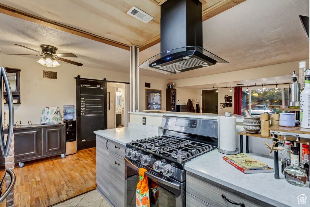 Kitchen with a ceiling fan, island exhaust hood, visible vents, stainless steel gas range oven, and a barn door