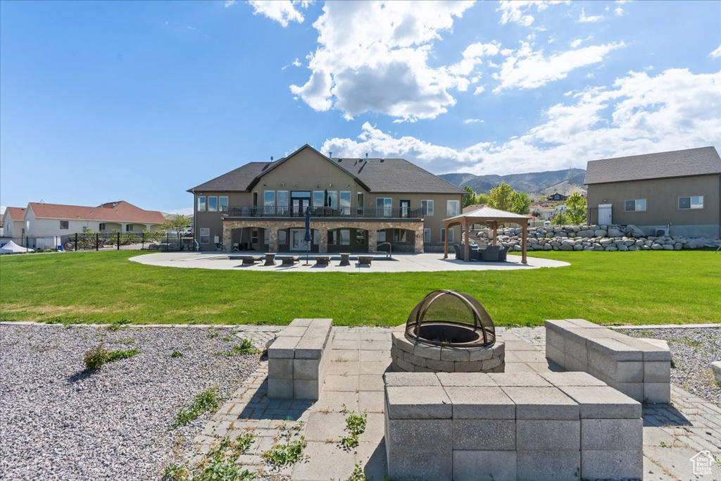 Rear view of property featuring a gazebo, a patio area, a balcony, a lawn, and a fire pit