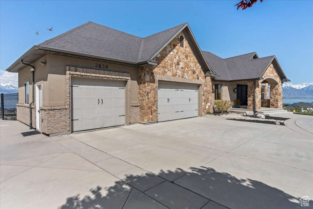 View of front facade featuring driveway, a garage, a mountain view, a shingled roof, and stone siding