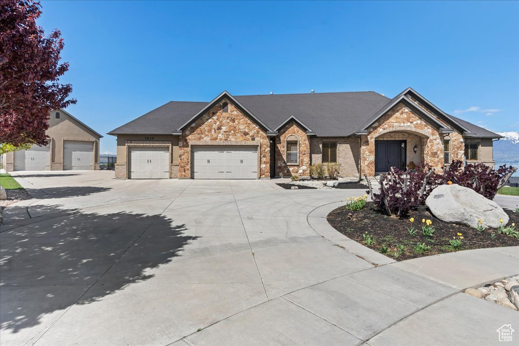 View of front facade with brick siding, driveway, stone siding, and a garage
