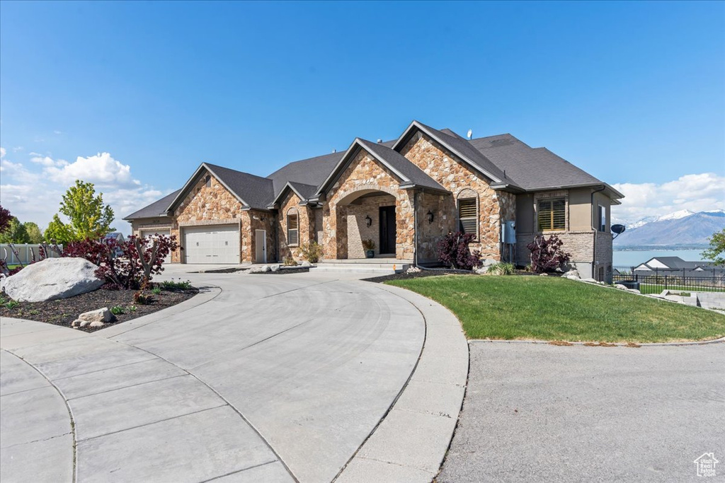 French country inspired facade featuring fence, a front lawn, stone siding, a garage, and curved driveway