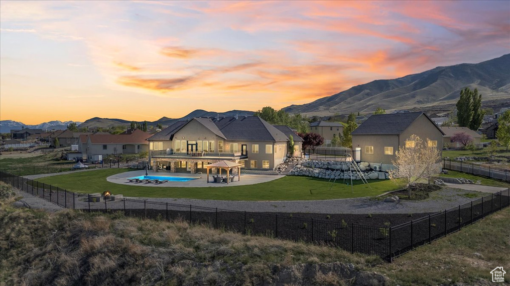 Back of house at dusk featuring a fenced in pool, a mountain view, a balcony, a fenced backyard, and a yard