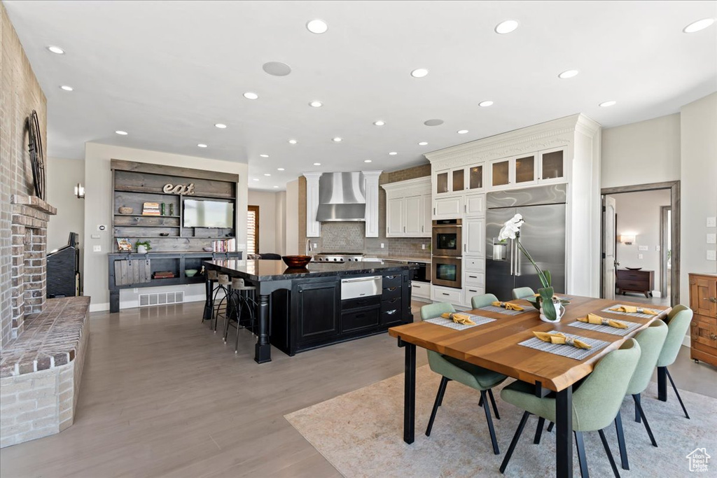 Dining area featuring a brick fireplace, recessed lighting, light wood-style flooring, and visible vents