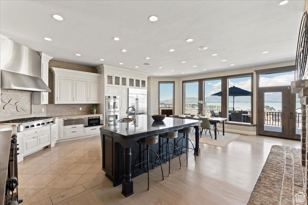 Kitchen featuring backsplash, a kitchen bar, a sink, built in appliances, and wall chimney exhaust hood
