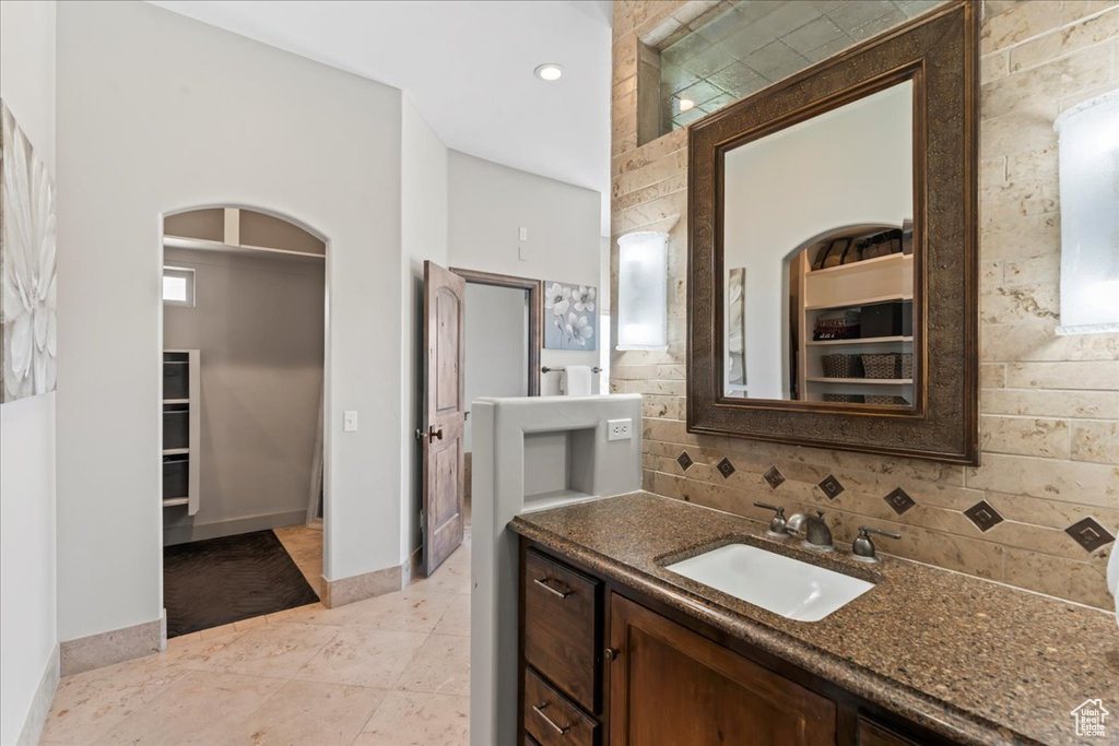 Full bathroom with tasteful backsplash, vanity, baseboards, tile patterned floors, and a spacious closet