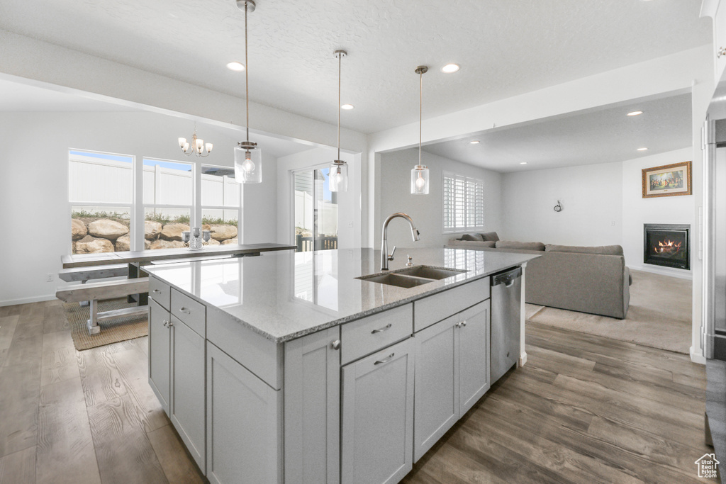 Kitchen with stainless steel dishwasher, wood finished floors, open floor plan, an island with sink, and a sink