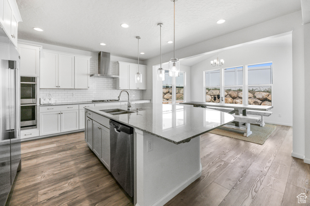 Kitchen featuring wall chimney range hood, backsplash, a sink, a chandelier, and stainless steel appliances