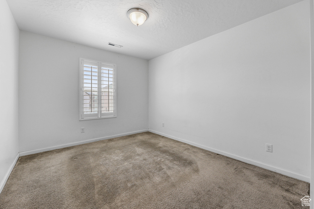 Carpeted empty room featuring visible vents, a textured ceiling, and baseboards