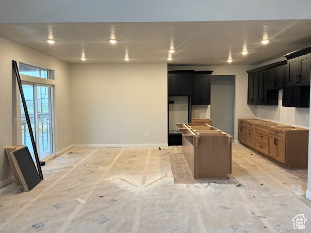 Kitchen with dark cabinets, a kitchen island, and baseboards
