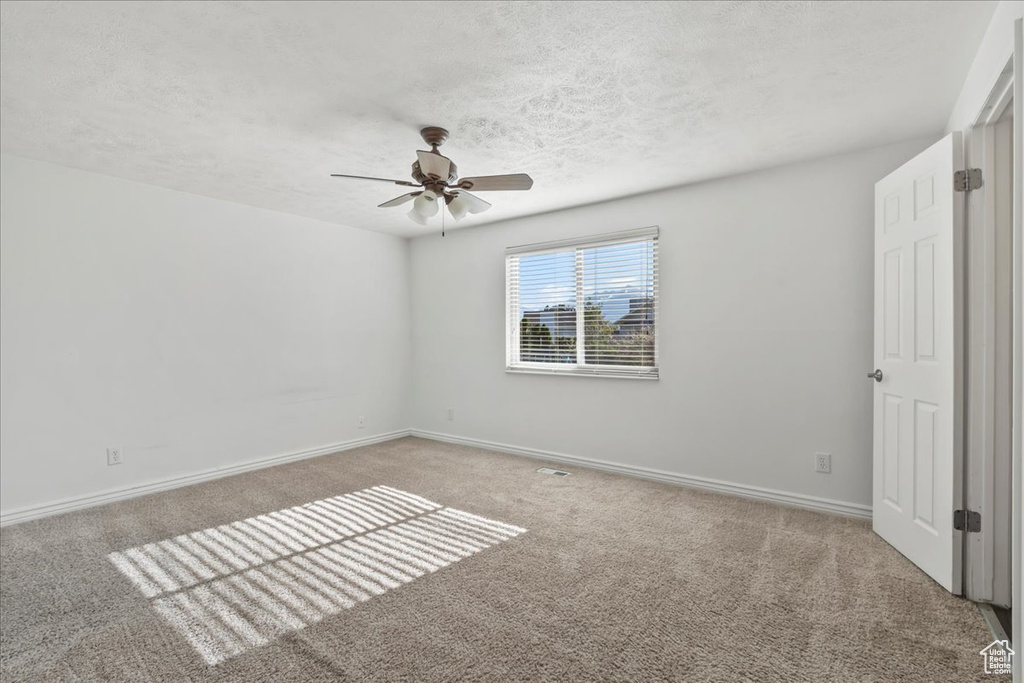 Carpeted empty room featuring a textured ceiling, ceiling fan, and baseboards