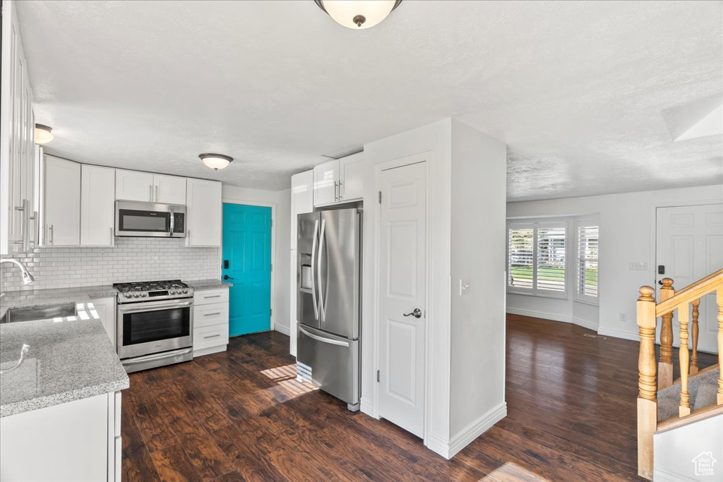 Kitchen with a sink, dark wood finished floors, stainless steel appliances, baseboards, and white cabinetry