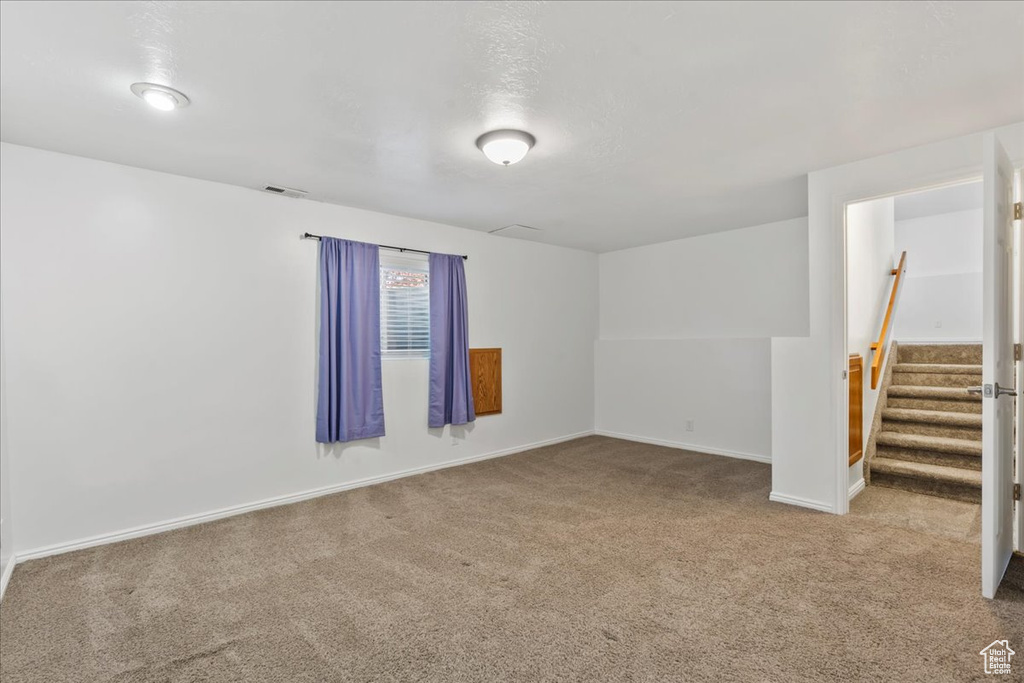 Unfurnished room featuring carpet floors, baseboards, stairs, and visible vents