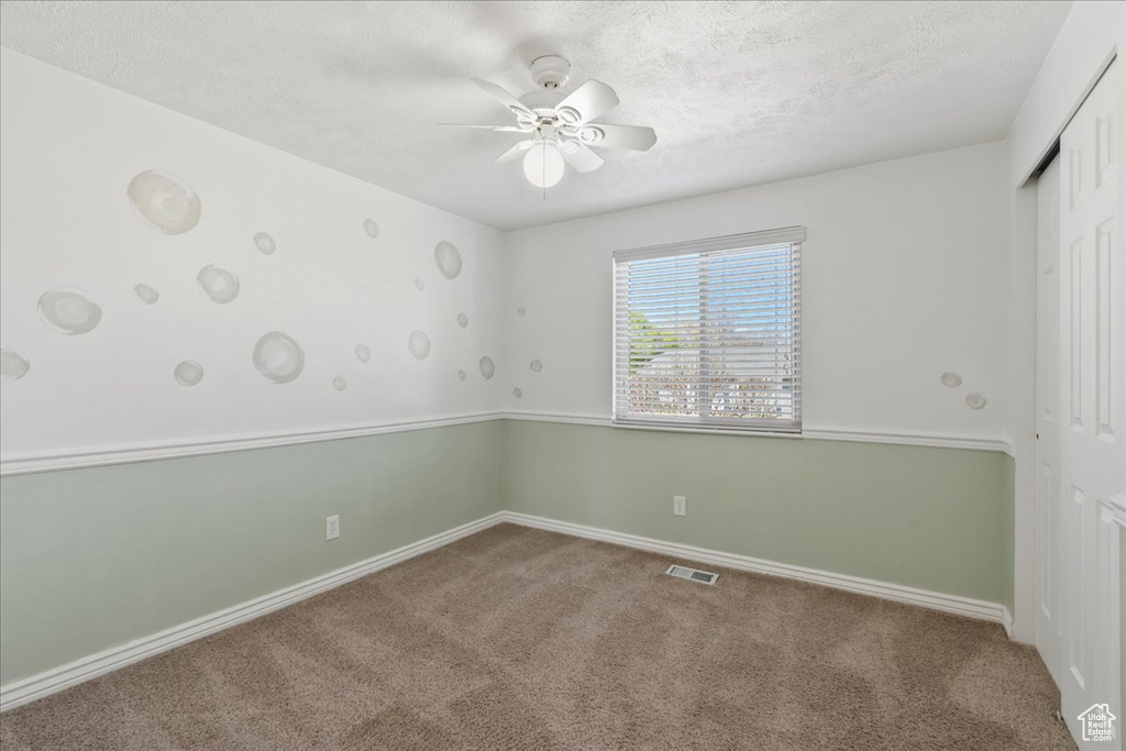 Carpeted empty room featuring a textured ceiling, ceiling fan, visible vents, and baseboards