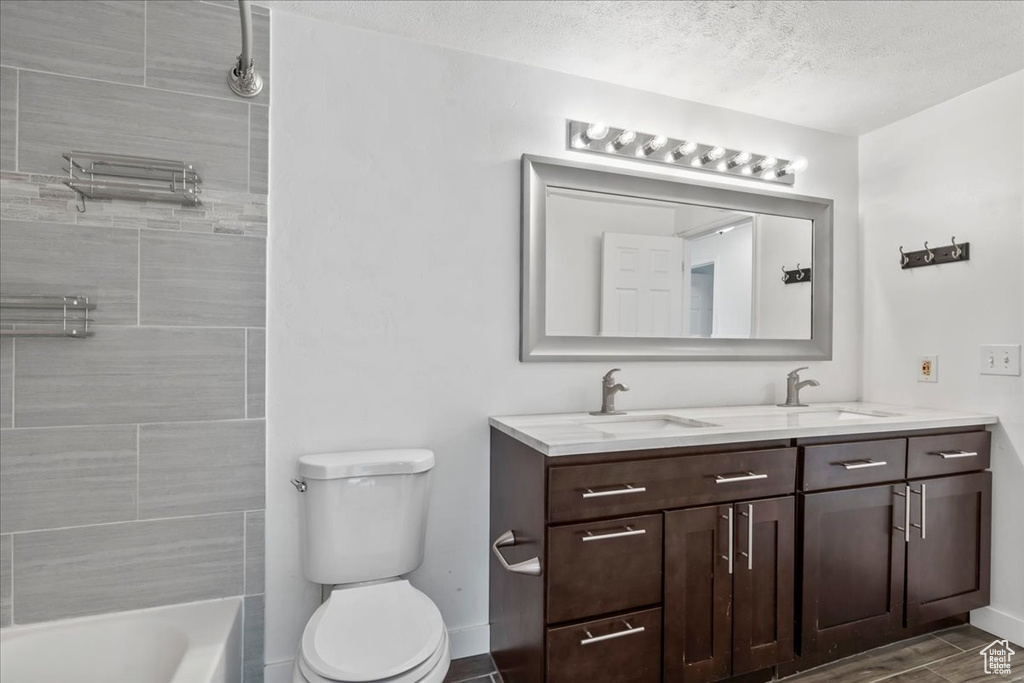 Bathroom featuring double vanity, a sink, a textured ceiling, and toilet