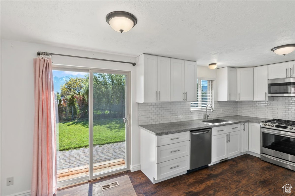 Kitchen featuring backsplash, visible vents, appliances with stainless steel finishes, a sink, and dark wood-style floors