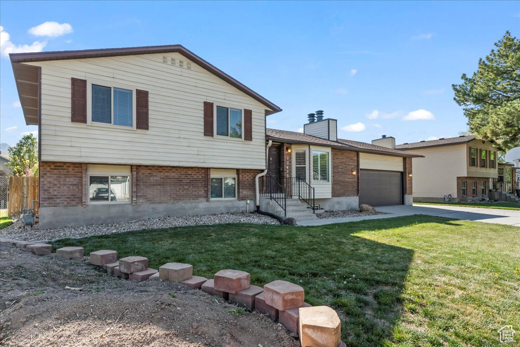 Split level home featuring a garage, concrete driveway, a front lawn, and brick siding