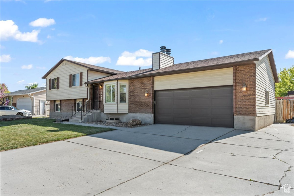 Tri-level home with a garage, a front lawn, a chimney, brick siding, and driveway