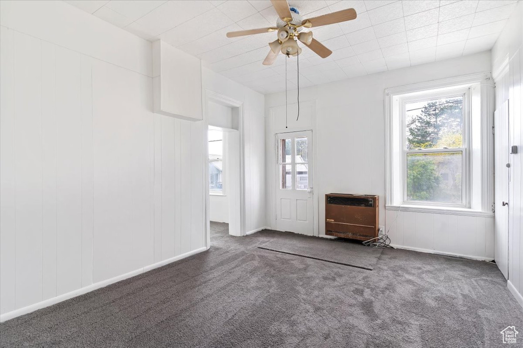 Carpeted spare room featuring heating unit and ceiling fan