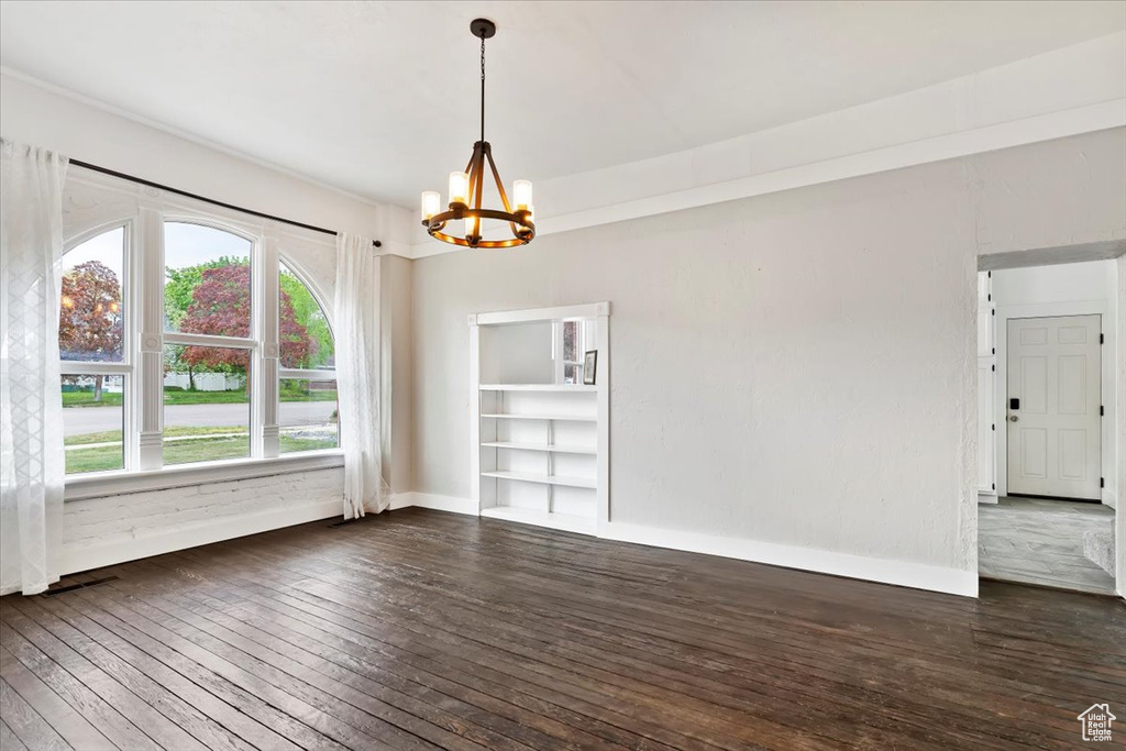 Unfurnished dining area featuring baseboards, dark wood-style flooring, and a chandelier