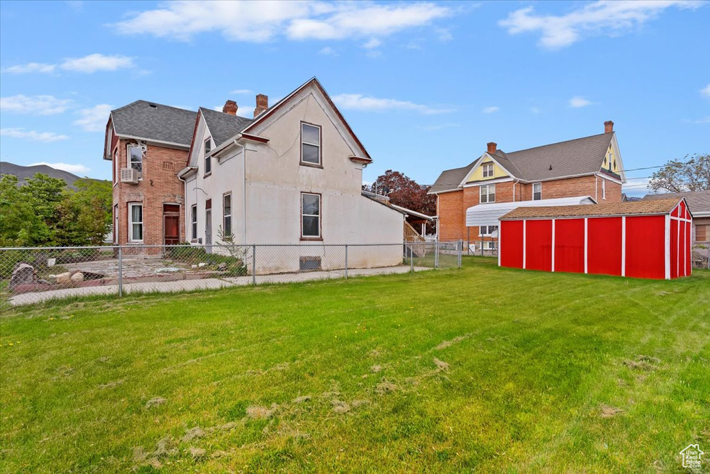 Back of property with a storage shed, fence, an outbuilding, and a yard