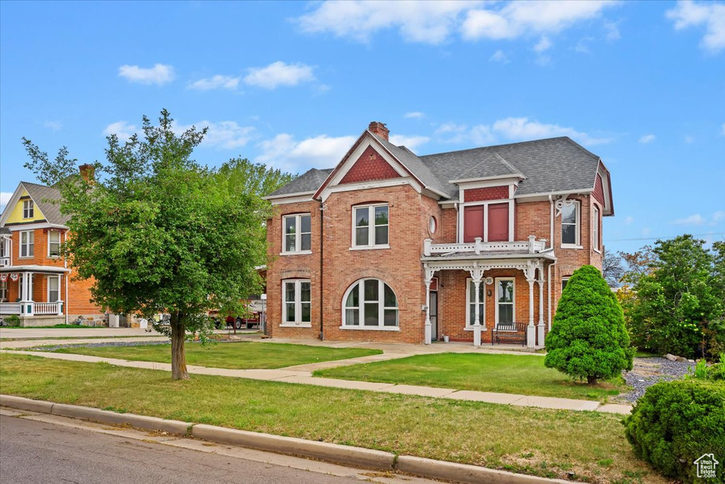 View of front of house featuring brick siding, a chimney, a shingled roof, and a front yard