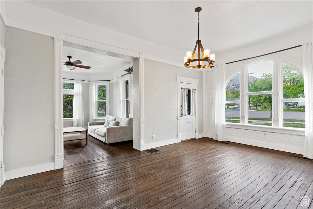 Unfurnished dining area with visible vents, dark wood finished floors, ceiling fan with notable chandelier, and baseboards