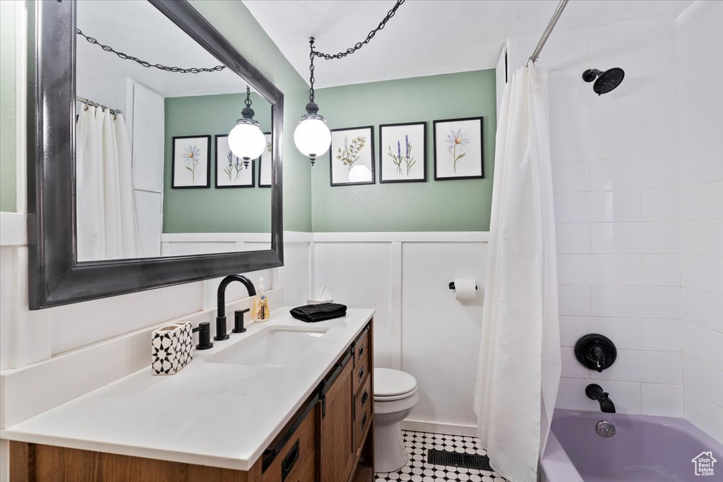 Bathroom featuring wainscoting, a decorative wall, vanity, toilet, and shower / tub combo