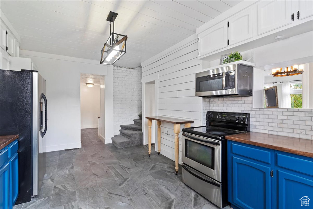 Kitchen featuring butcher block counters, baseboards, white cabinetry, stainless steel appliances, and blue cabinetry