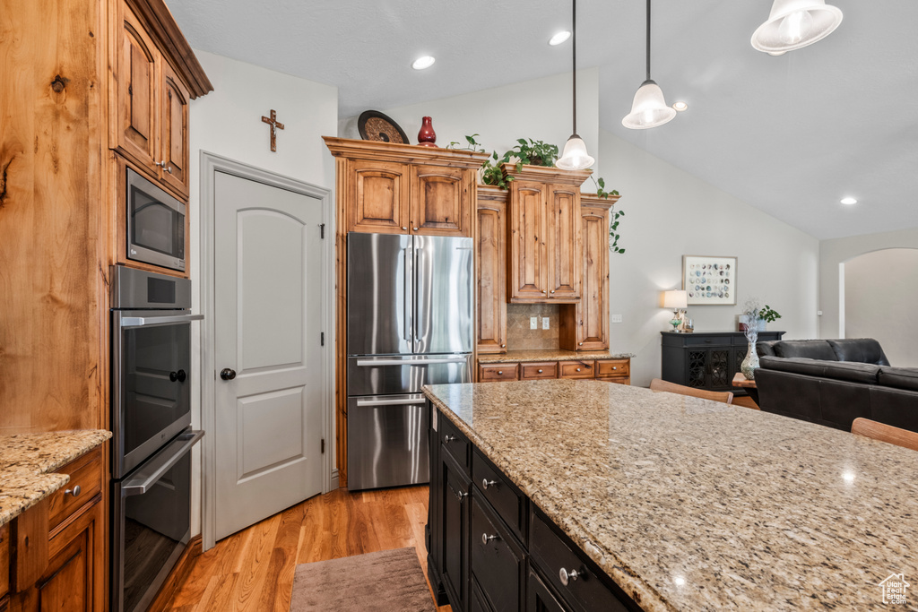 Kitchen featuring light stone countertops, arched walkways, light wood-style flooring, stainless steel appliances, and vaulted ceiling