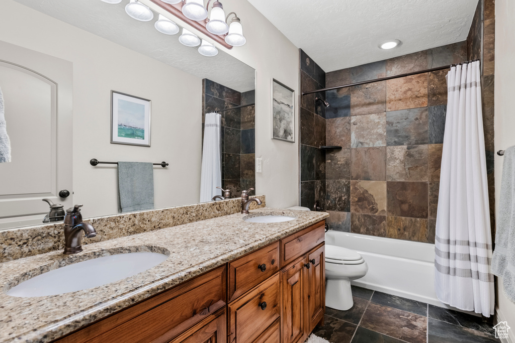 Full bathroom featuring double vanity, toilet, shower / bath combination with curtain, and a sink