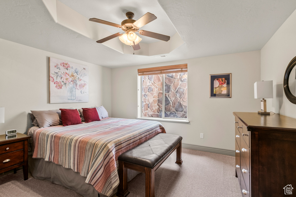 Carpeted bedroom with baseboards, visible vents, ceiling fan, and a raised ceiling