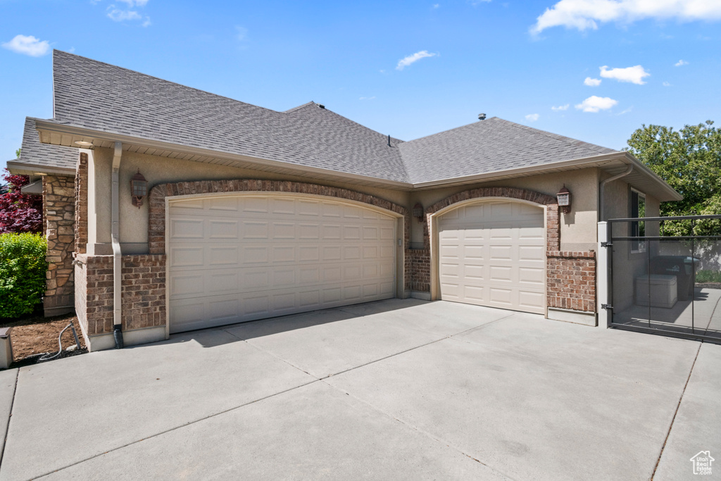 Exterior space with a shingled roof, an attached garage, stone siding, a gate, and concrete driveway