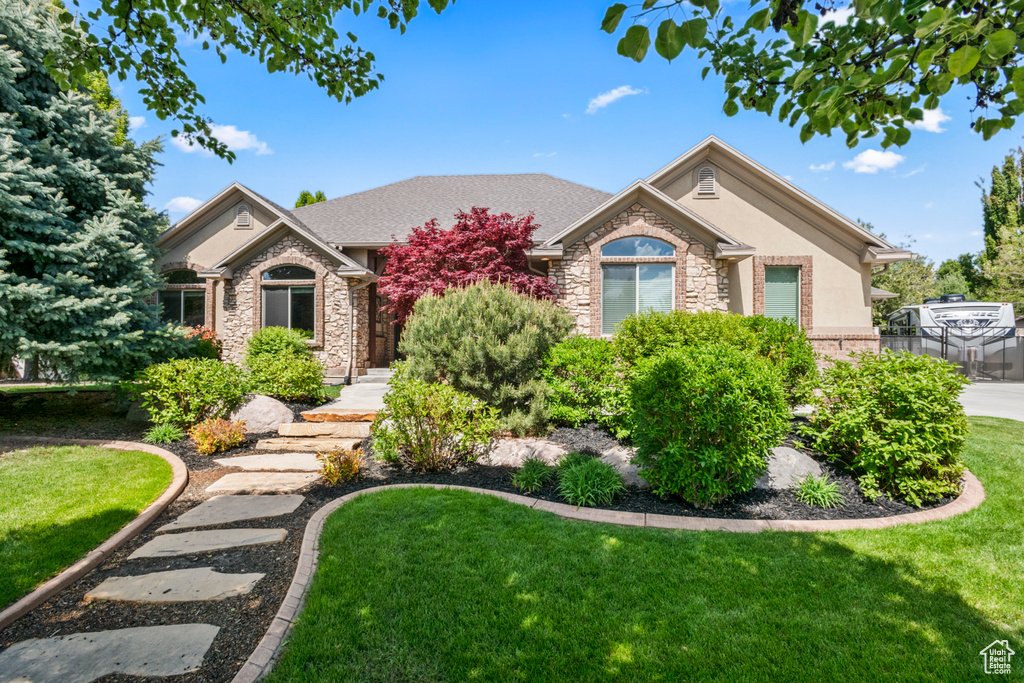 Single story home featuring a front lawn, stucco siding, and stone siding