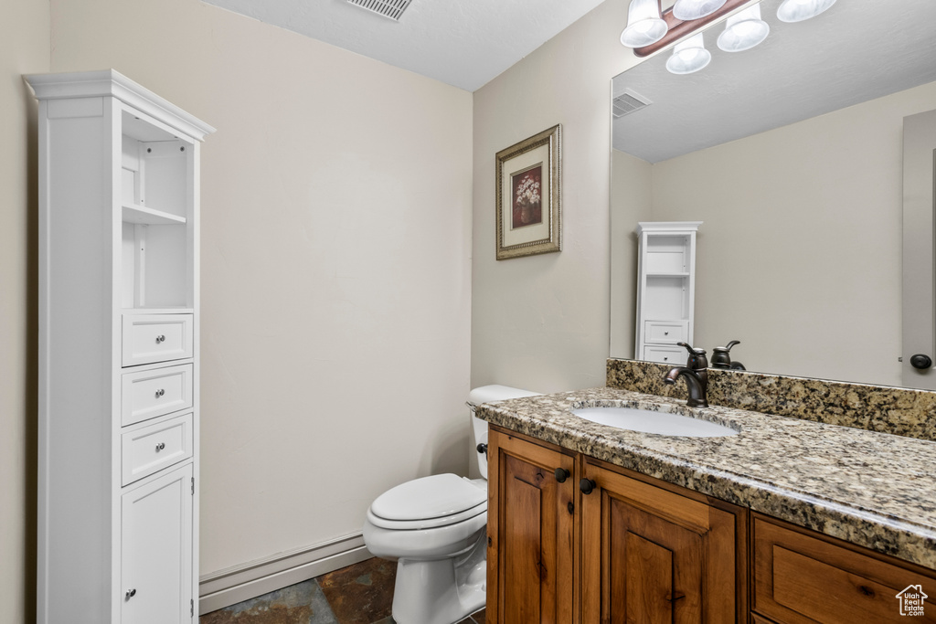 Half bath featuring toilet, a baseboard heating unit, visible vents, and vanity