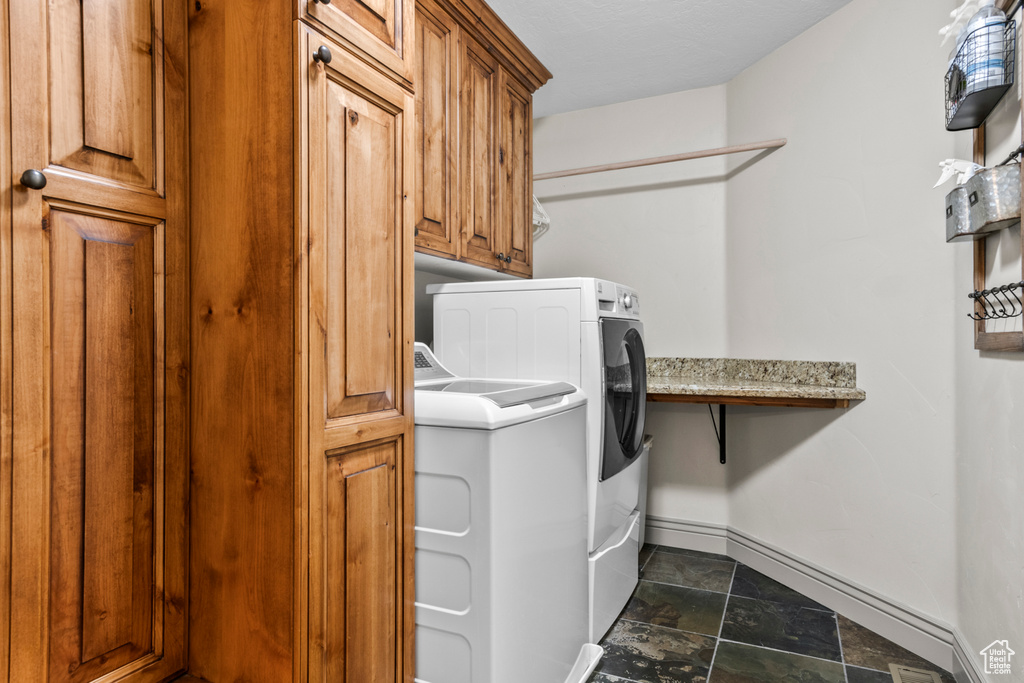 Washroom with cabinet space, baseboards, washing machine and dryer, and stone finish floor